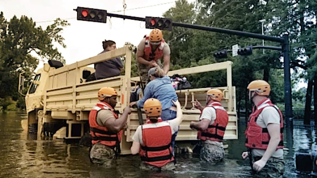 Volunteers help a woman into the bed of a truck on a flooded street.