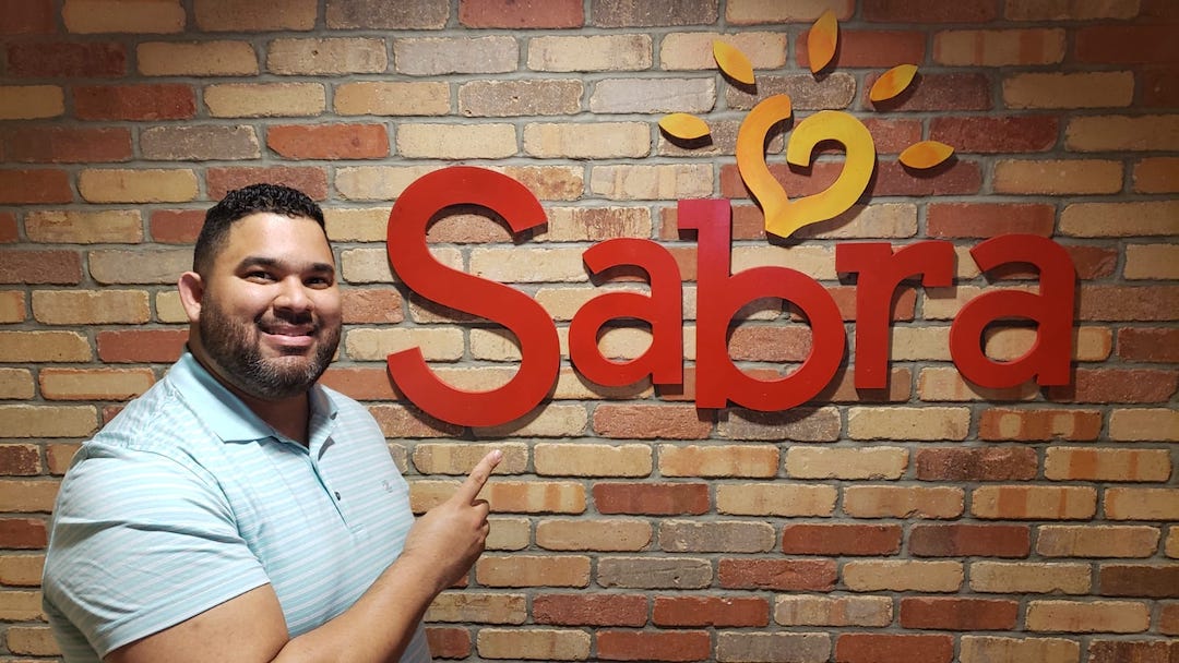 Juan Vargas, PMP, in front of a Sabra sign on the company's corporate offices.